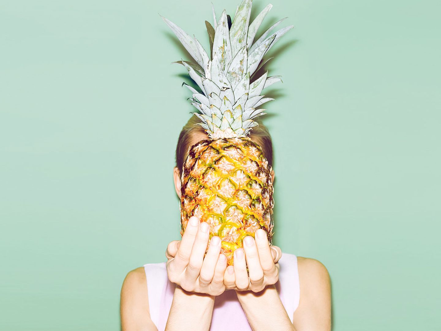 Eine Frau hält sich eine Ananas vor das Gesicht