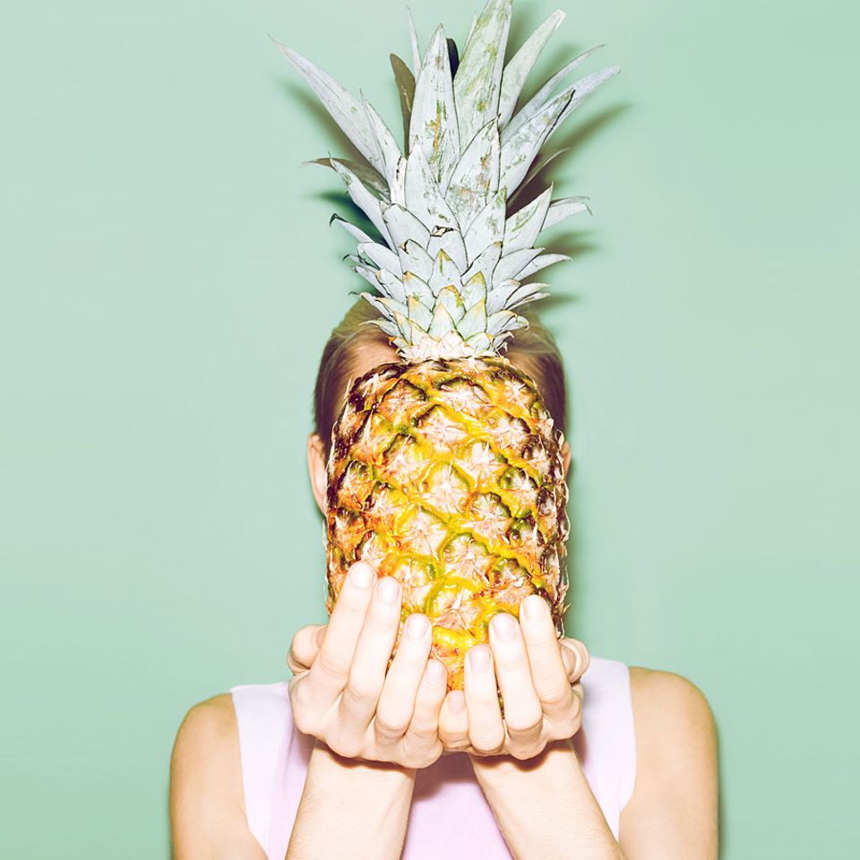 Eine Frau hält sich eine Ananas vor das Gesicht