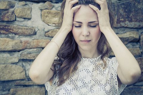 Regelschmerzen: Leidende Frau hält sich den Kopf