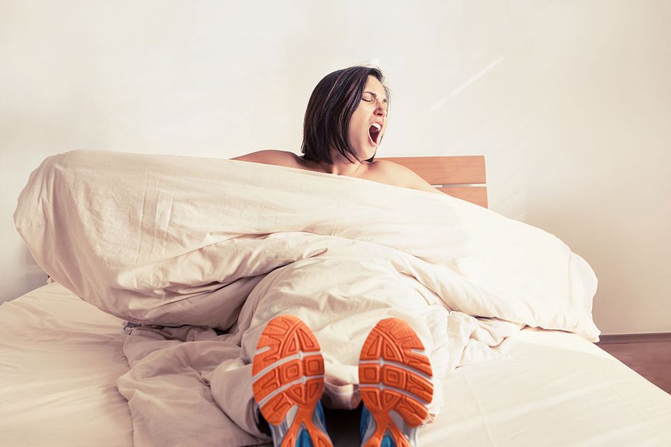 Fitnessübungen fürs Bett: Frau mit Turnschuhen liegt im Bett