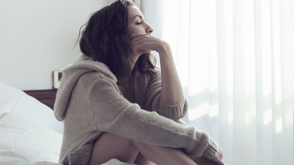7 Gründe, warum deine Periode zu spät kommen kann: Frau sitzt auf dem Bett