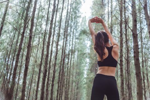 Rückenfett loswerden: Frau dehnt sich beim Sport im Wald