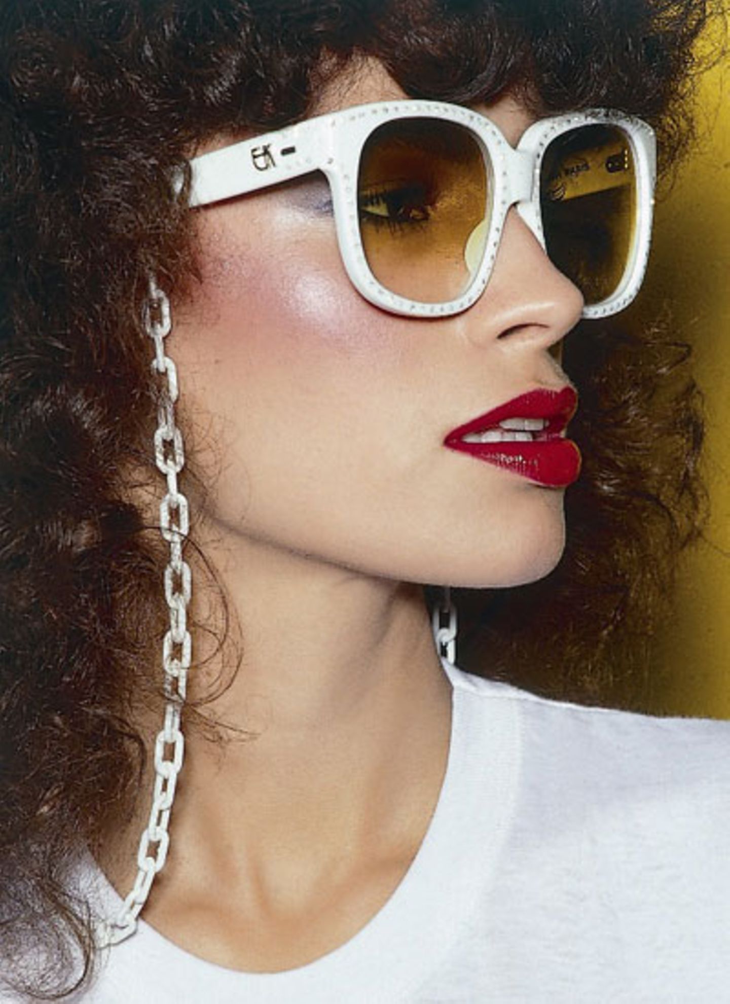 Das brasilianische Model Rio trägt eine weiße Retro-Sonnenbrille mit Brillenkette und rotem Lippenstift.