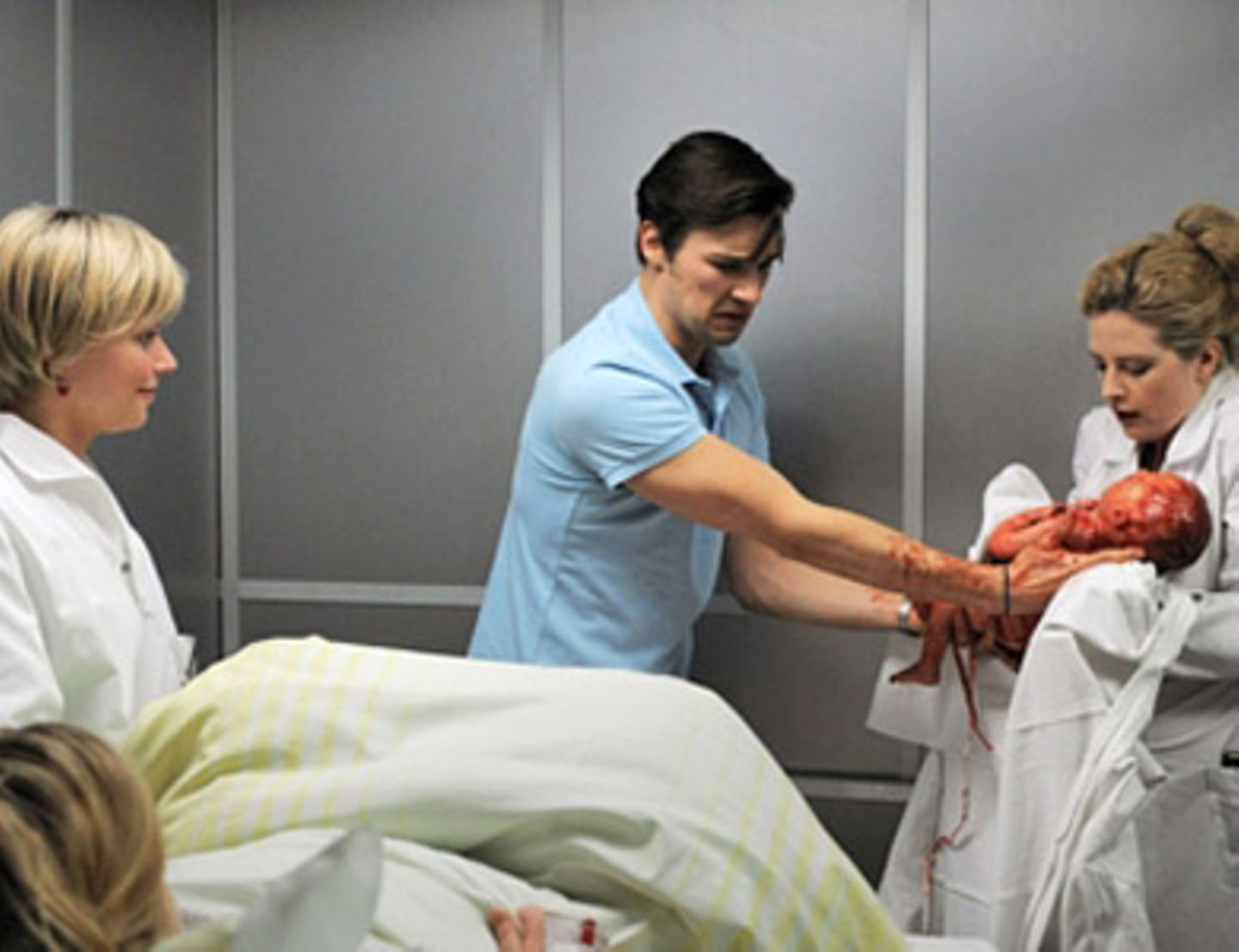Geburt im Fahrstuhl. Marc Meier (Florian David Fitz) übergibt das Neugeborene an Gretchen Haase (Diana Amft, re.). Schwester Sabine (Annette Strasser) ist stolz auf ihren Oberarzt.