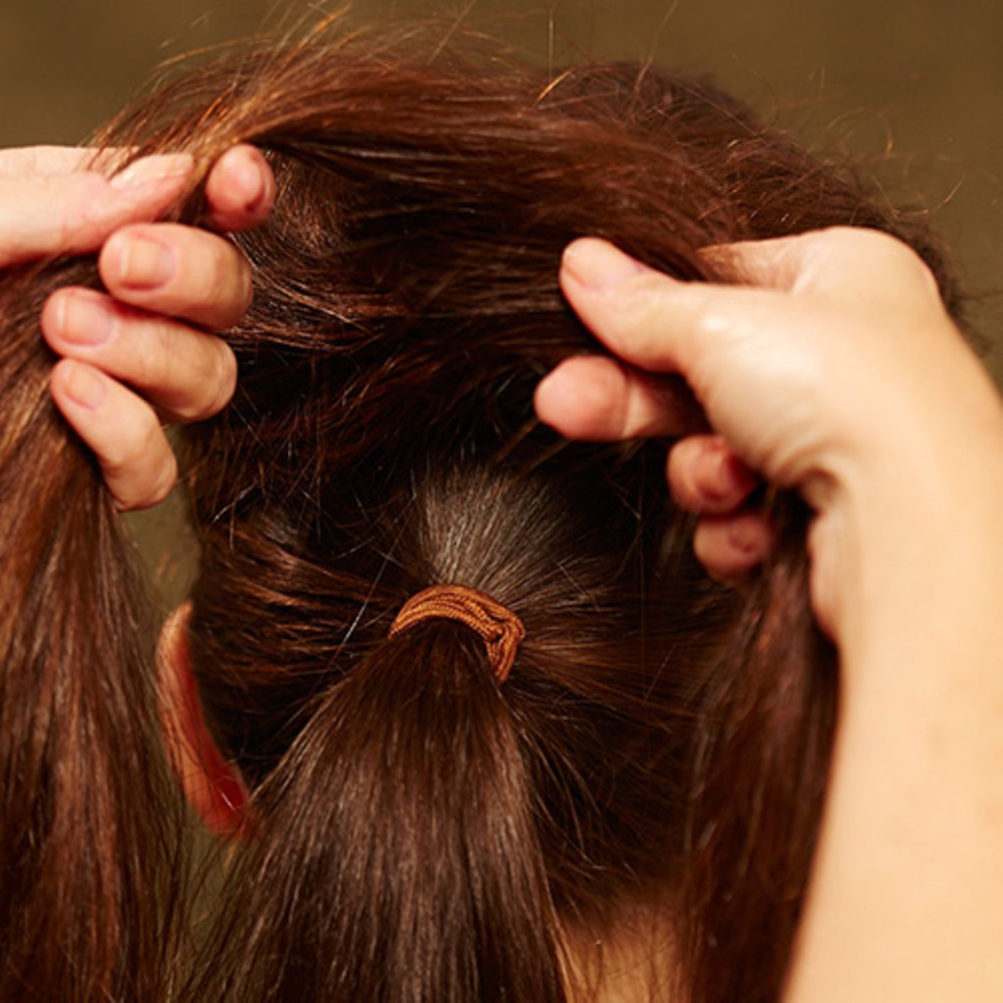 Die Haare am Oberkopf leicht antoupieren, mit Haarspray besprühen. Die aufgebauschten Partien mit den Fingern ein wenig glätten, dann in zwei Stränge einteilen.