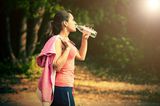 Gesunde Ernährung: Frau im Sport-Outfit trinkt Wasser aus der Flasche