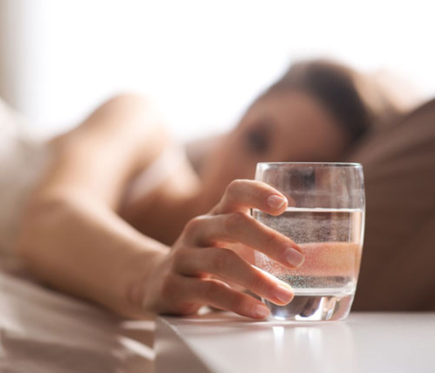 Schnelle Fettverbrenner: Eine Frau greift im Bett zu einem Wasserglas
