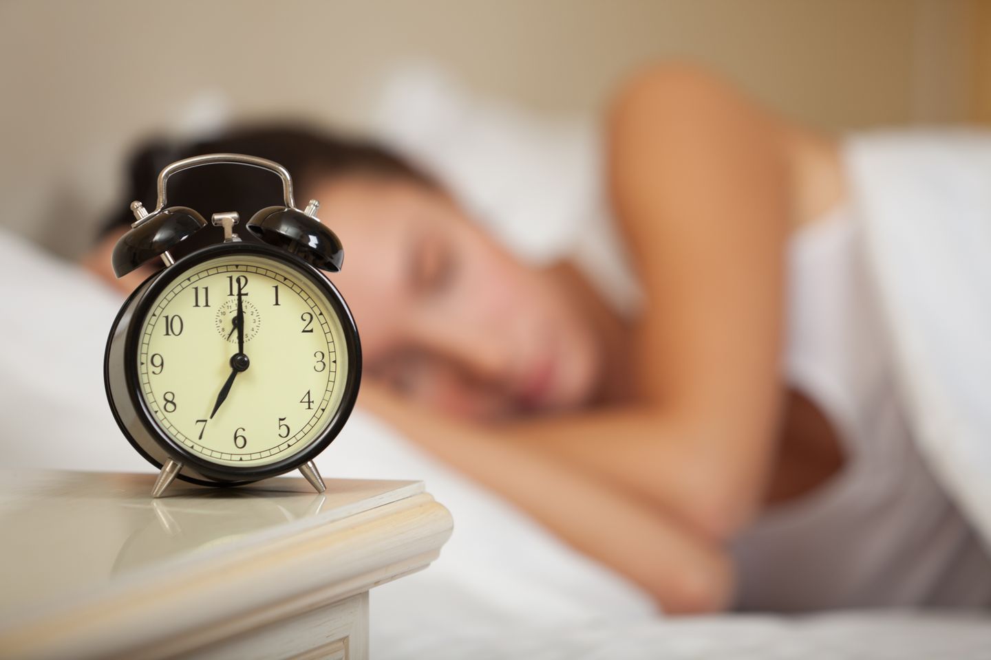 Schnelle Fettverbrenner: Eine Frau liegt schlafend im Bett, im Vordergrund ein Wecker, der 7 Uhr anzeigt