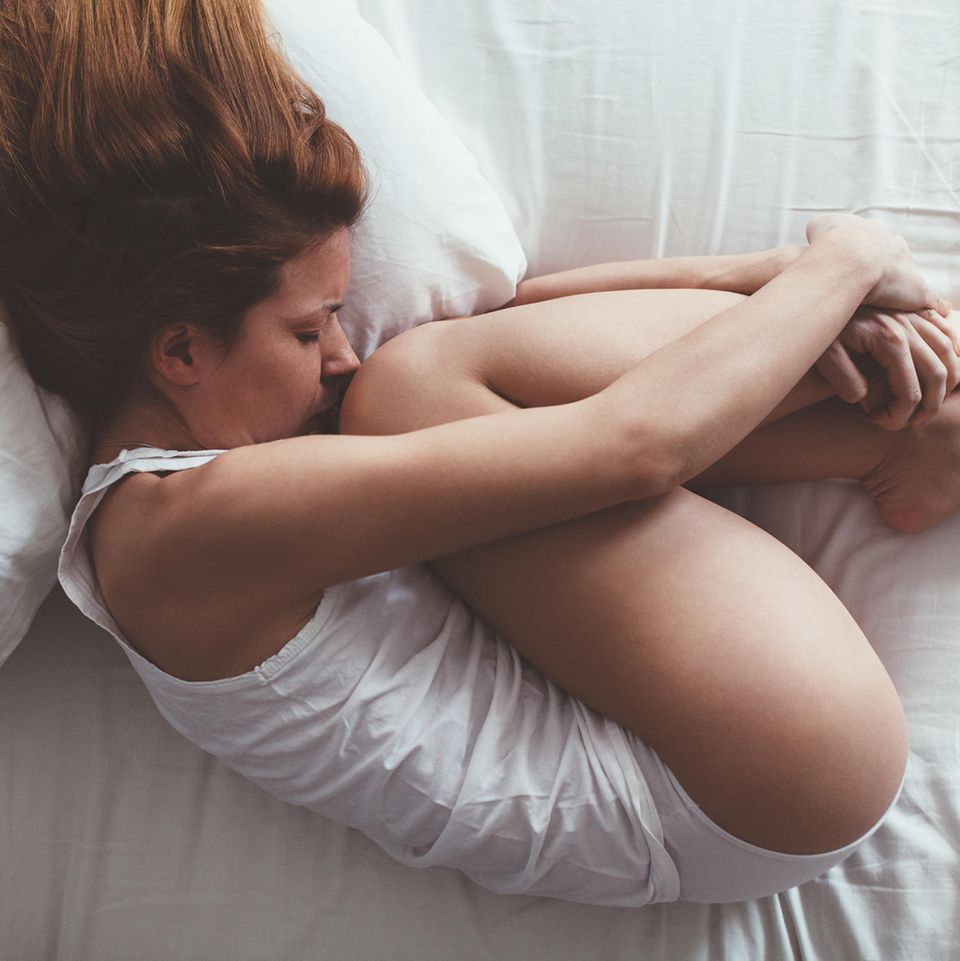 Scheidenkrampf: Eine Frau liegt zusammengerollt auf ihrem Bett
