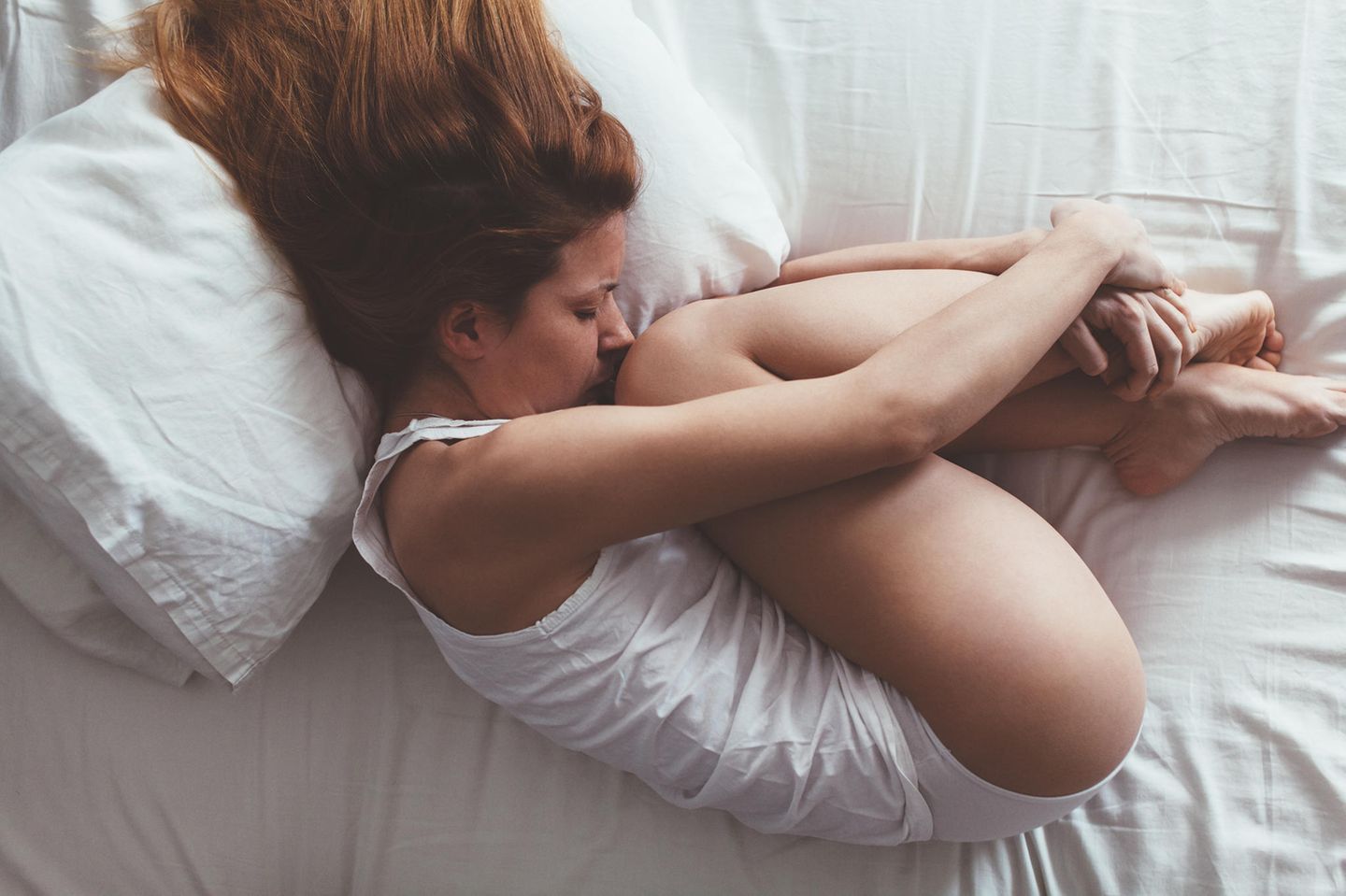 Scheidenkrampf: Eine Frau liegt zusammengerollt auf ihrem Bett