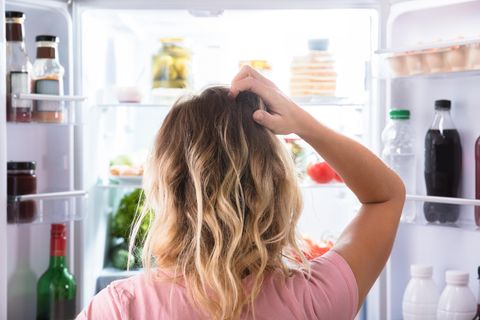 Eine Frau steht vor dem Kühlschrank und kratzt sich am Kopf.