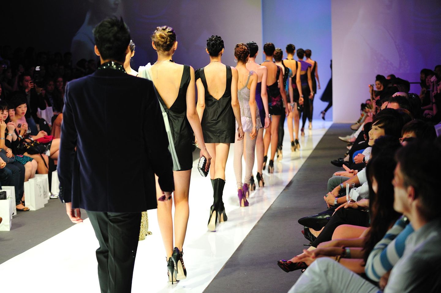 Models laufen auf einem Laufsteg vor Publikum.