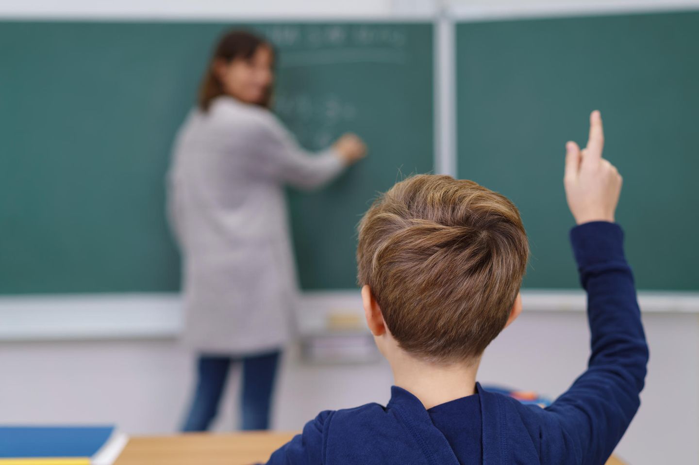 Ein Junge hebt in einem Klassenzimmer die Hand.