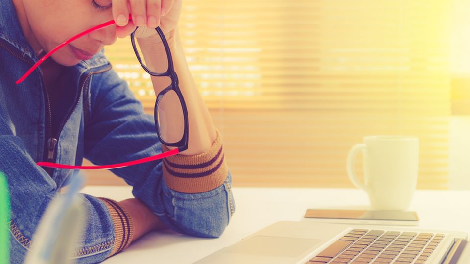 Krank durch Job: So stark ist der Einfluss Krank durch Job: Frau sitzt erschöpft im Büro