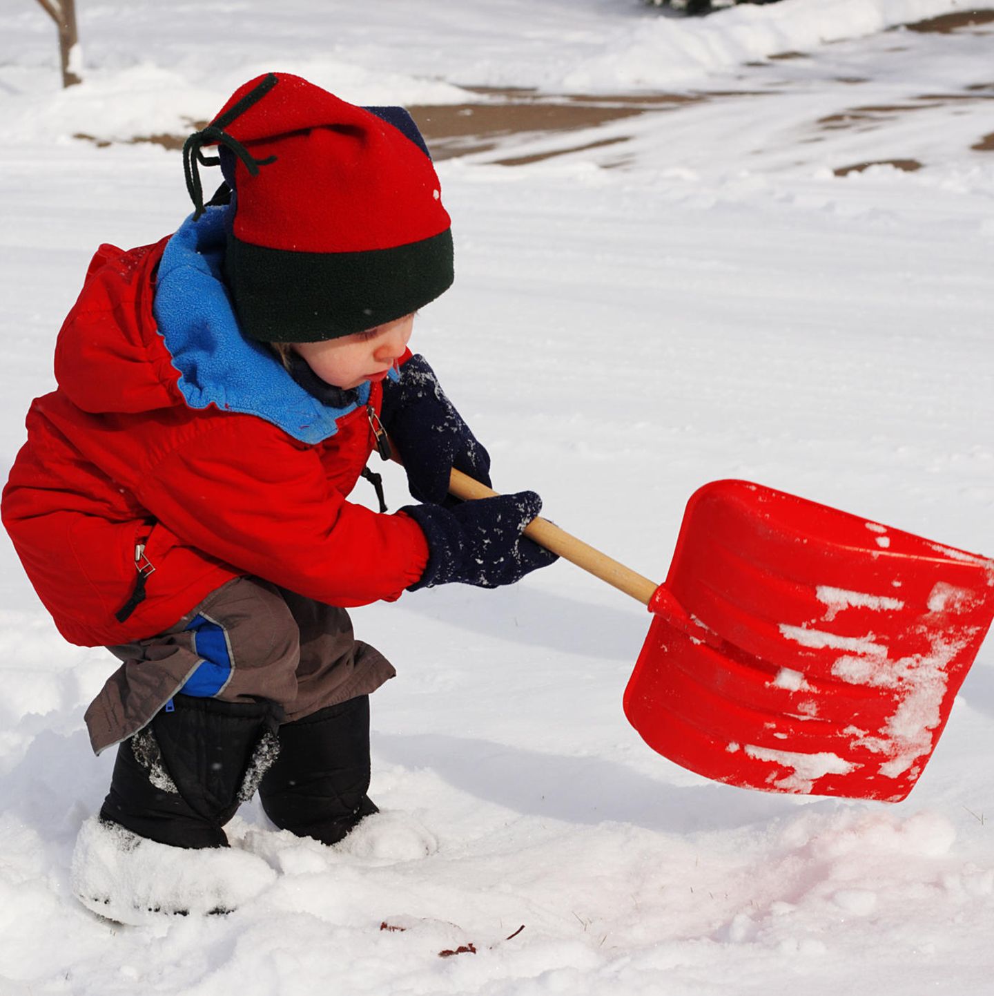 Kind mit Stiefeln im Schnee mit Schippe