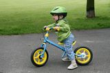 Kind auf Laufrad mit Helm und festen Schuhen