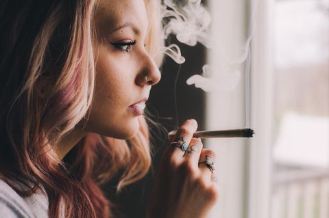 Cannabis legalisieren? Frau raucht Joint am Fenster
