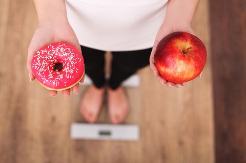 Montignac-Methode: Frau hält in der einen Hand einen Donut und in der anderen einen Apfel