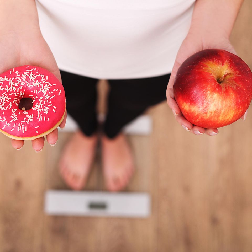 Montignac-Methode: Frau hält in der einen Hand einen Donut und in der anderen einen Apfel