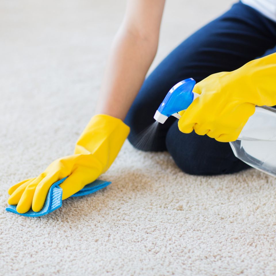 Teppich reinigen: Frau kniet auf Teppich und entfernt Flecken