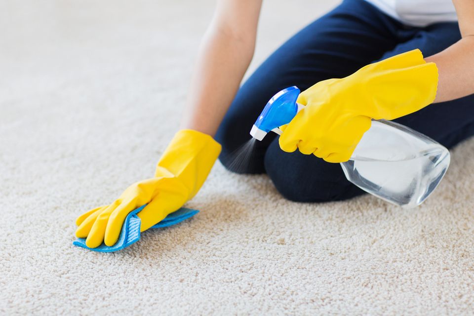 Teppich reinigen: Frau kniet auf Teppich und entfernt Flecken