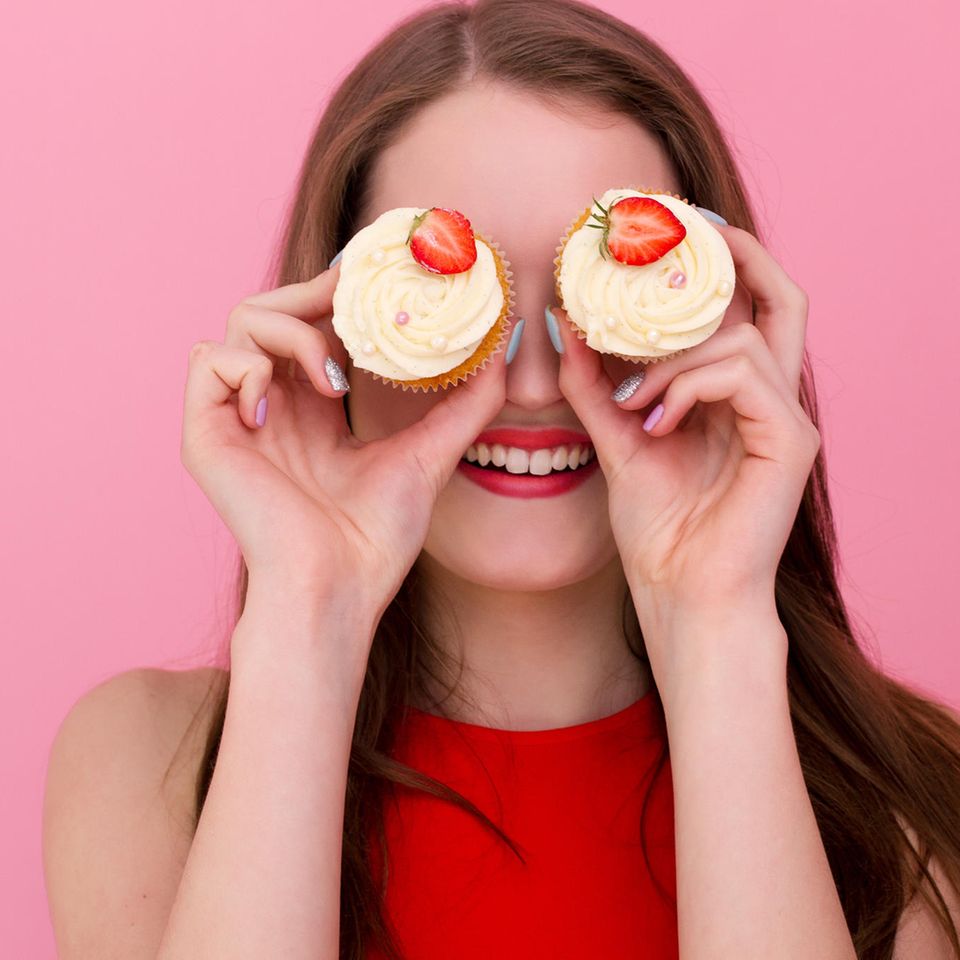 FdH: Frau hält sich zwei Cupcakes mit Erdbeeren vor die Augen, grinst
