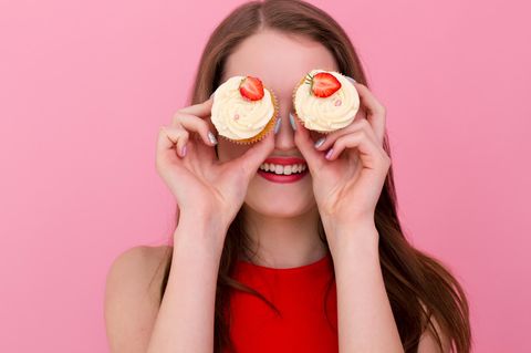 FdH: Frau hält sich zwei Cupcakes mit Erdbeeren vor die Augen, grinst