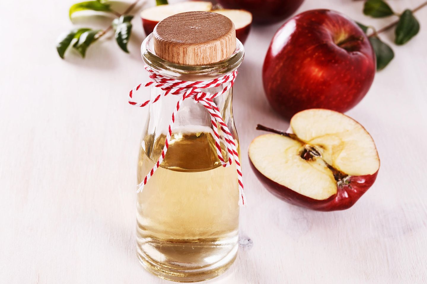 Apfelessig-Diät: Apfelessig in einer Glasflasche, daneben drapierte Äpfel