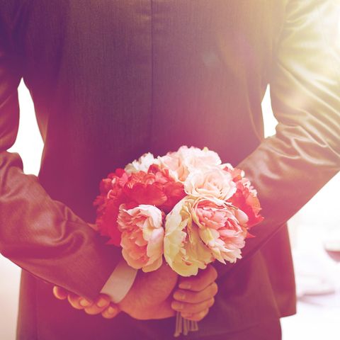 Hochzeitstage: Mann hält Blumen hinter seinem Rücken