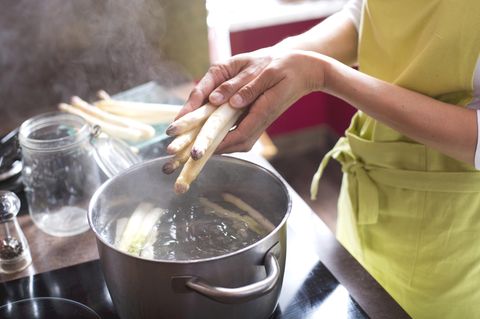 Spargel-Kochzeit: Frau legt Spargel in einen Topf