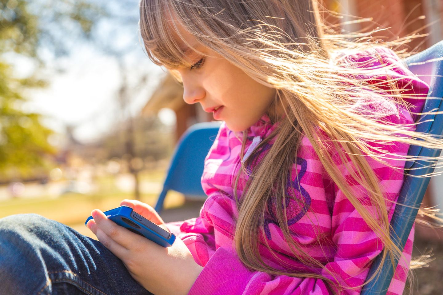 Trauer: Ein kleines Mädchen mit einem Handy auf einer Bank im Park