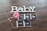 Liebevoll drapierte Ultraschallbilder als Flatlay auf Tisch mit Blume und dem Wort Baby