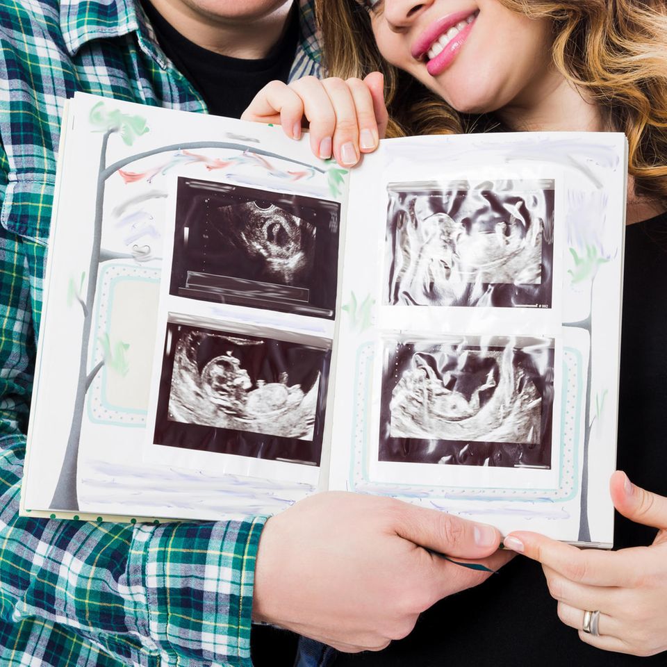 Eltern haltend bunt bemaltes Buch mit eingeklebten Ultraschallbildern in die Kamera