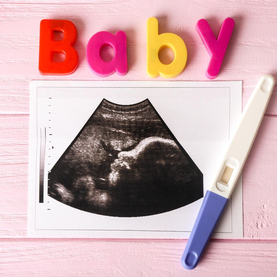 Ultraschallbild mit Schwangerschaftstest und Baby aus Buchstaben auf rosa Unterlage.