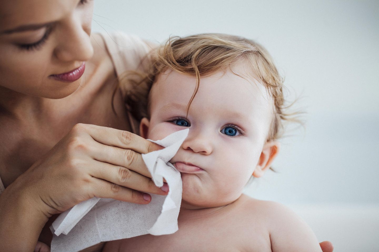 Mutter wischt Gesicht von Baby mit Feuchttuch sauber