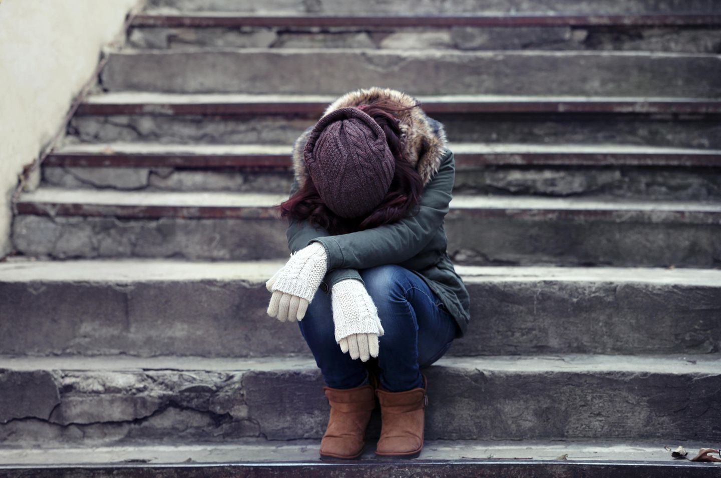Depression: Eine junge Frau sitzt mit gesenktem Kopf auf einer Steintreppe