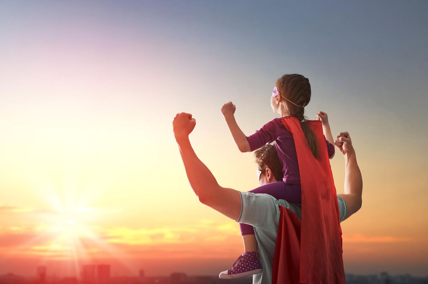 Vater hat Tochter auf Schultern und beide tragen Superheldenkostüme