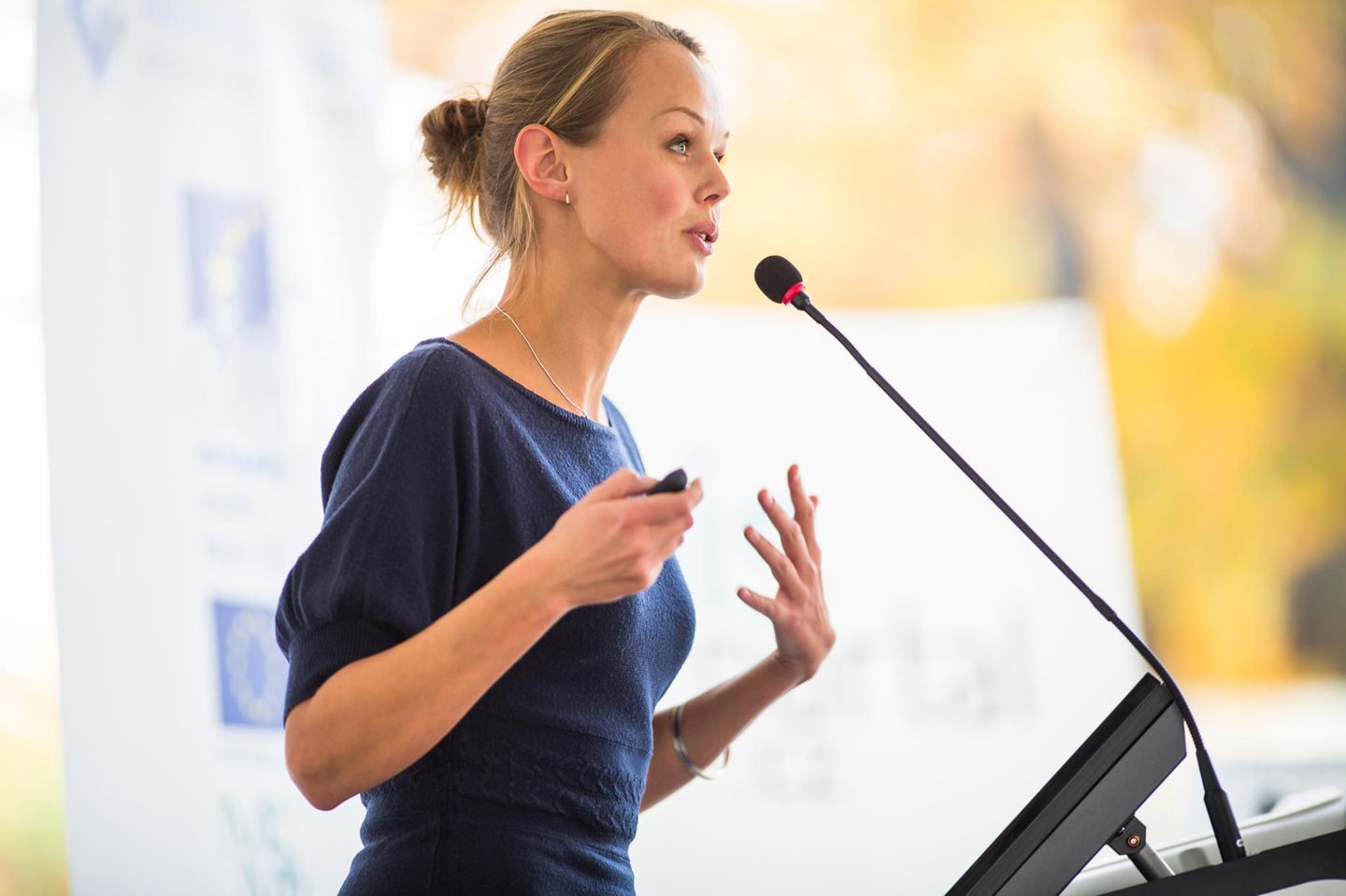 Karriere-Tipps für Frauen: Eine blonde Frau hält eine Rede am Rednerpult mit Mikro