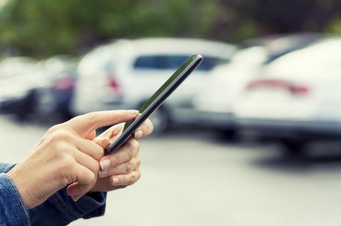 Falschparker-App: Eine Frau mit einem Smartphone auf einem Parkplatz