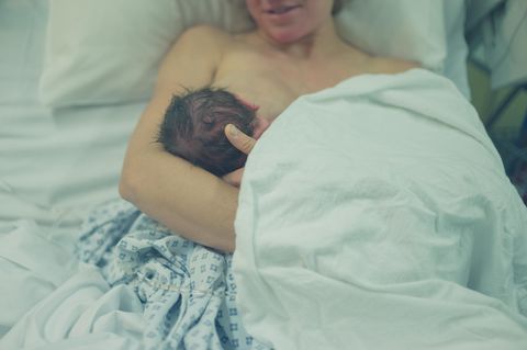 Mutter hält Neugeborenes fest im Arm und stillt es