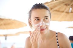 Sunburn on the face: woman creams her face on the beach