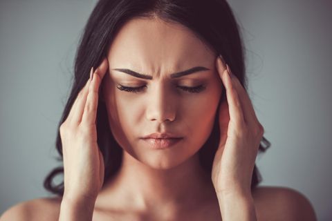 Kopfschmerzen: Frau mit schmerzverzerrtem Gesicht hält sich die Hände an die Stirn