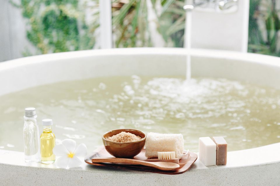Badewanne läuft ein, Badezusätze und Seifen stehen am Rand Badewanne läuft ein, Badezusätze und Seifen stehen am Rand