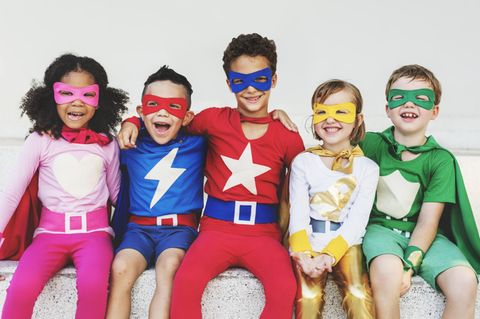 Kinder unterschiedlichen Alters in Superhelden-Kostümen beim Rumalbern