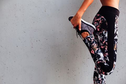 Diese Übungen sorgen für straffe Beine: Frau stretcht sich an grauer Wand