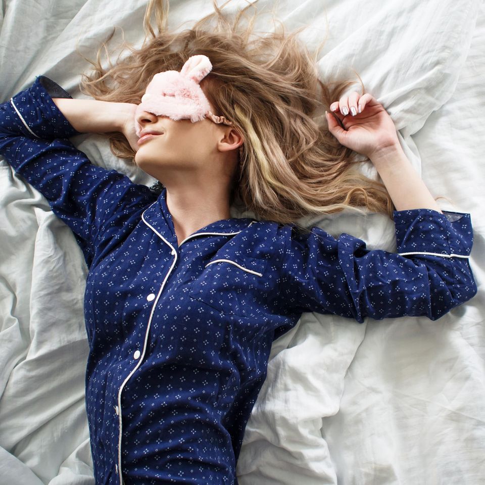 Warum du nicht auf der rechten Seite schlafen solltest: Frau mit Pyjama und Schlafmaske liegt im Bett