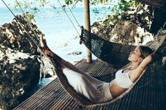 Reich werden: Diese Frau genießt eine Auszeit in einer Hängematte Reich werden: Frau liegt am Meer in Hängematte