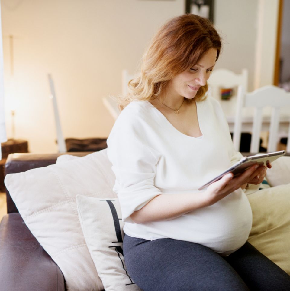 39. SSW: Schwangere sitzt mit Tablet auf dem Sofa