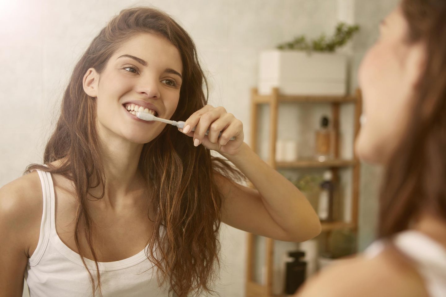 Mandelsteine entfernen: Frau putzt sich vor dem Spiegel die Zähne