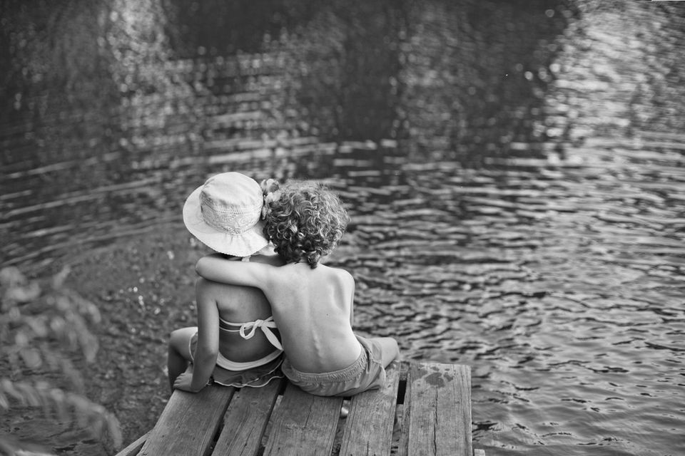 Zwei Kinder sitzen Arm in Arm an einem See